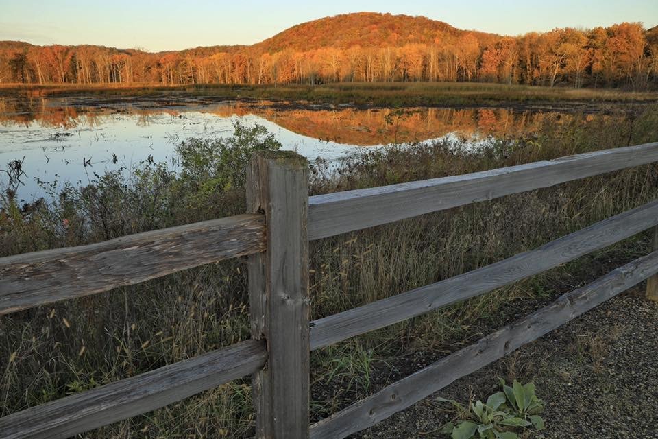 View of the Wisconsin Riverway over a split rail fence and a hill in the background.